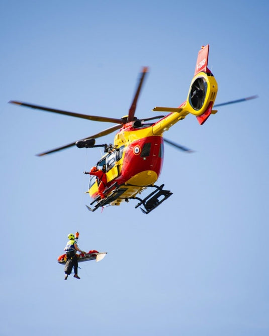 Rescue helicopter in the Alps hoisting a rescuer and a patient in a litter