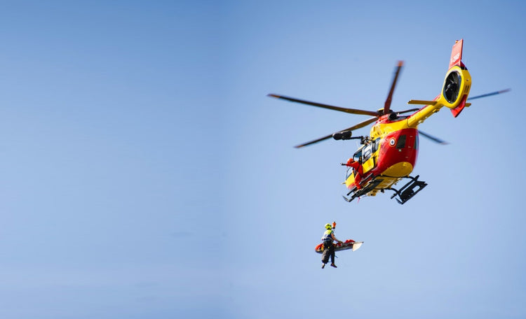 Rescue helicopter in the Alps hoisting a rescuer and a patient in a litter