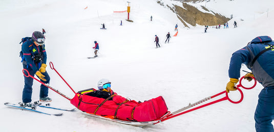 Ski patrol pulling an injured skier down the slope in a rescue sled
