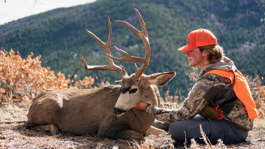 Hunter in blaze orange beside a mule deer buck