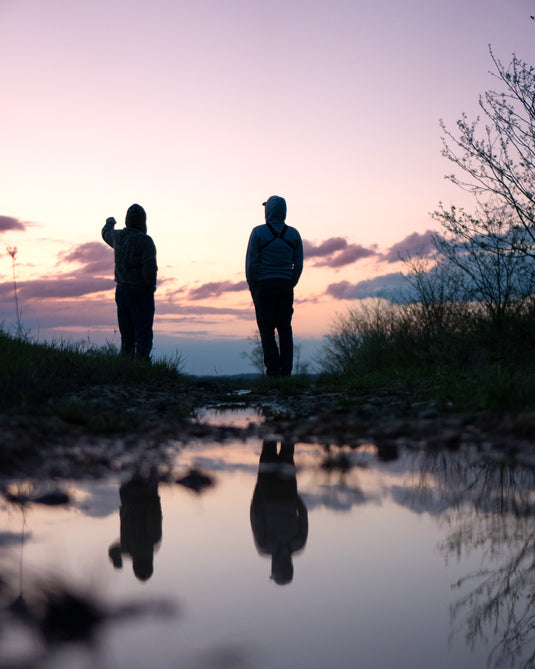 Two people at the edge of a lake at sunset